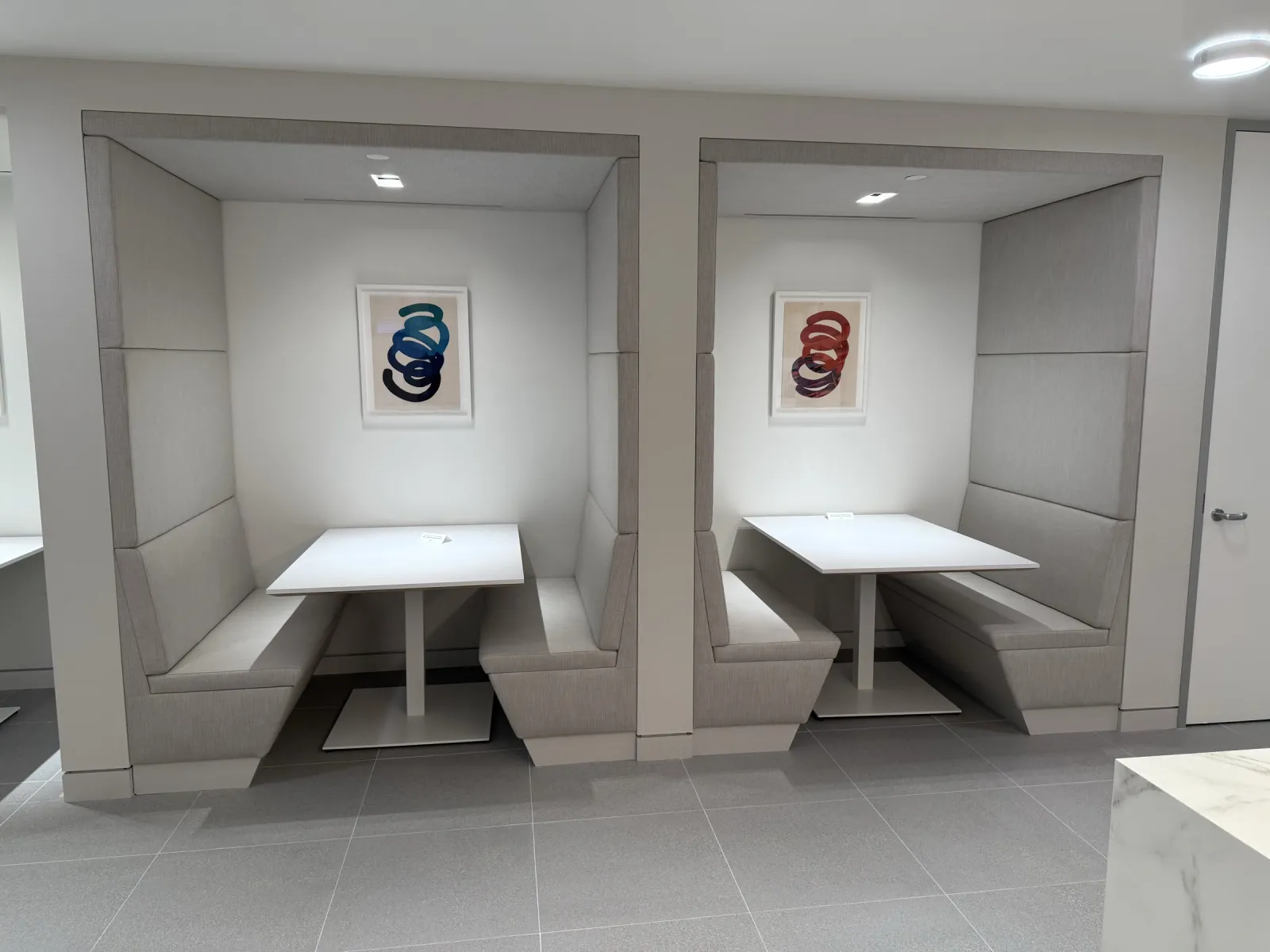 Two upholstered booth enclosures with white tables in the office break area