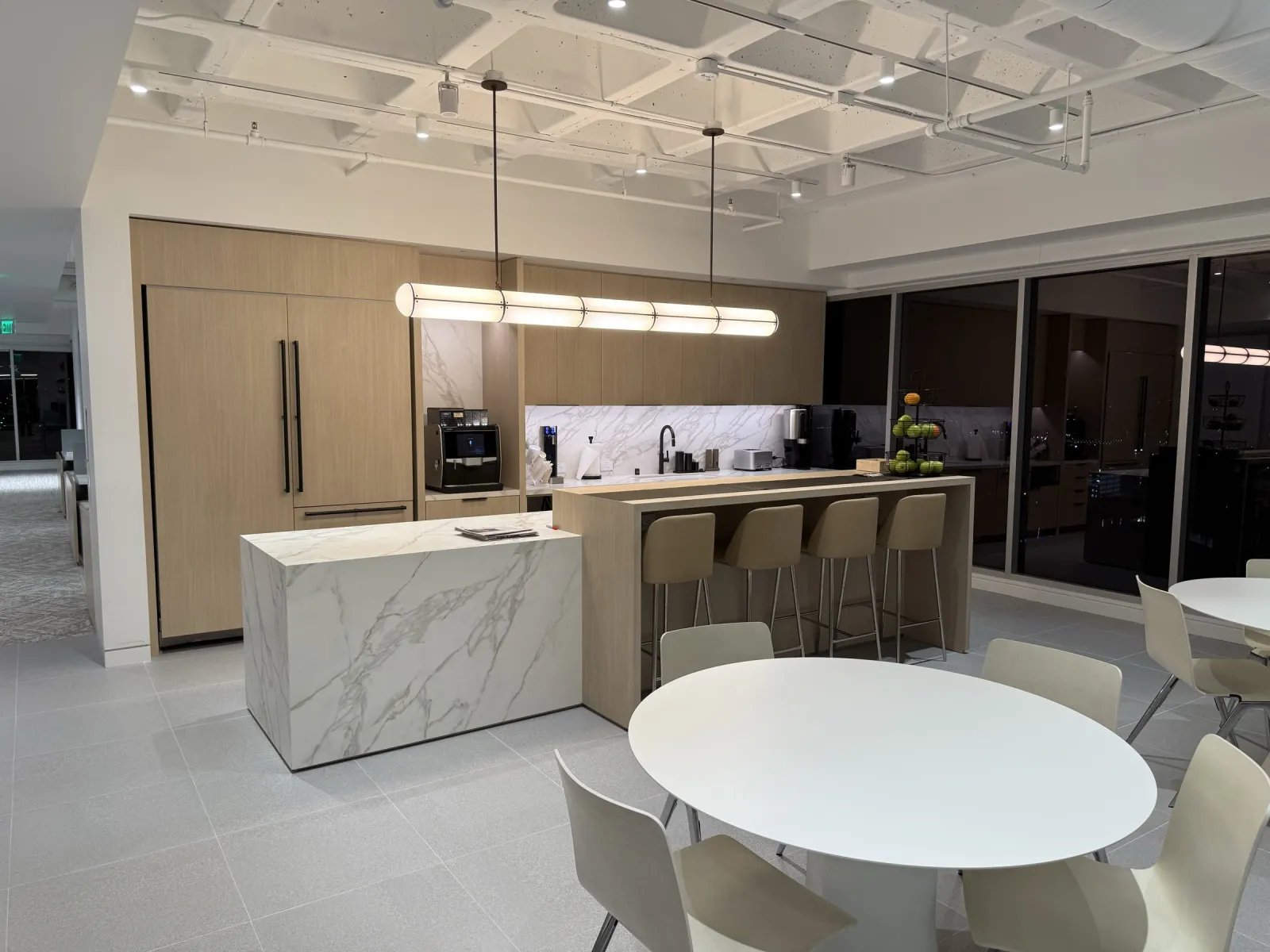 Light wood-grain break-area wall cabinetry, a wood island with bar stools and a marble-look island at Eastdil Secured's office