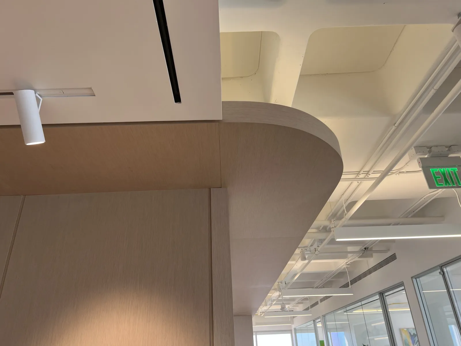 Curved wood-grain soffit wrapping the corner above the reception wall panels and into the corridor