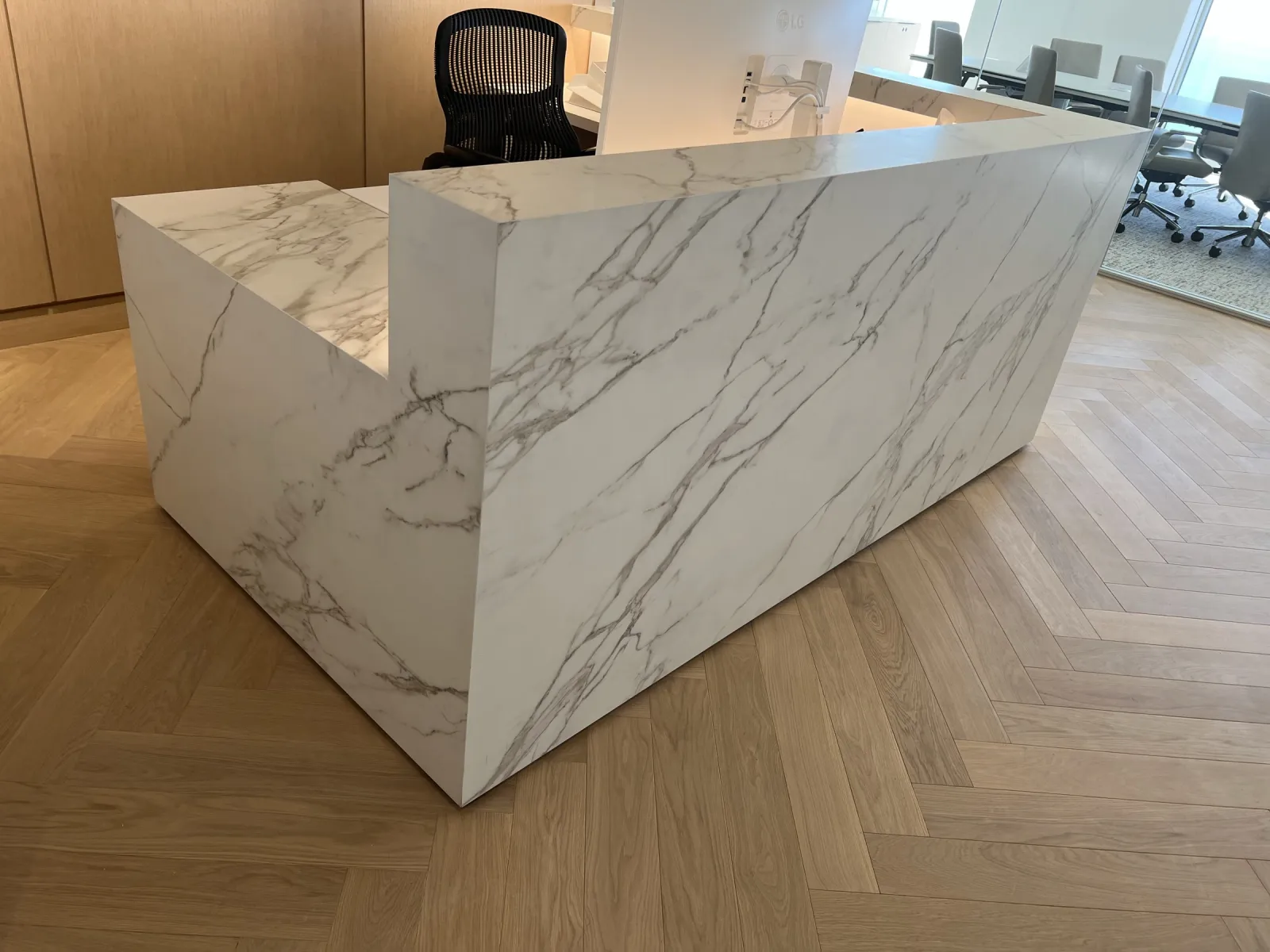 L-shaped reception desk clad in marble-look panels on a herringbone wood floor at Eastdil Secured