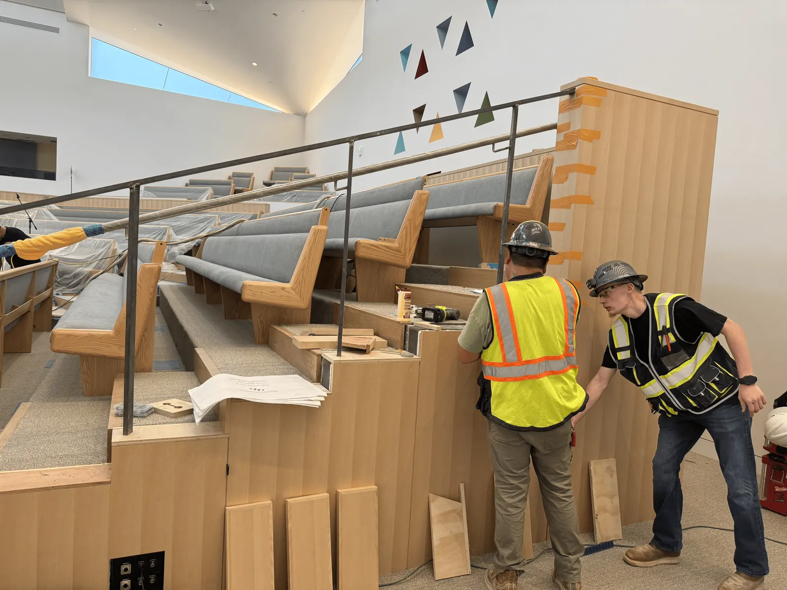 Installers fitting light wood panels in Kehillat Israel's sanctuary, with the pews under protective covering