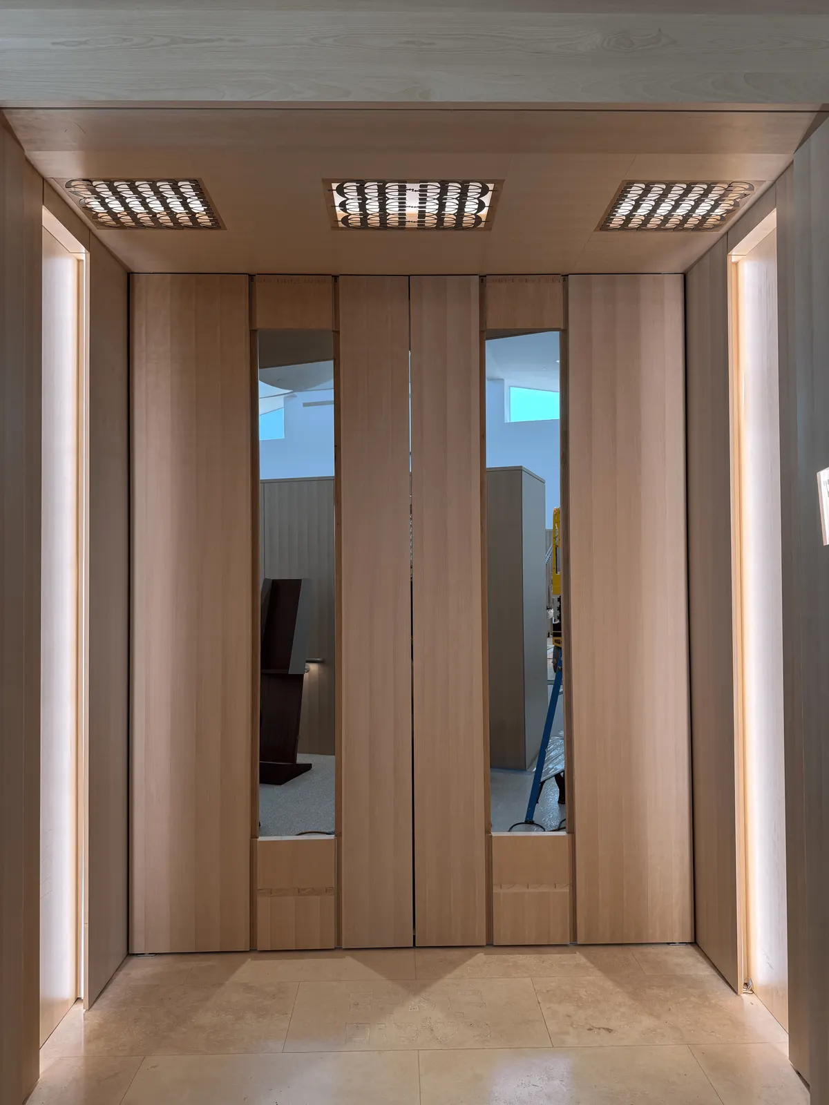 Wood pivot doors with tall glass inserts inside the Portal, under patterned ceiling light panels