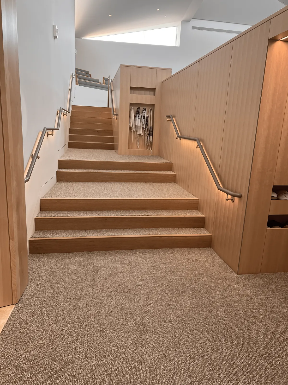 Synagogue stair lined with vertical wood wall paneling, a lit handrail and a recessed wood niche