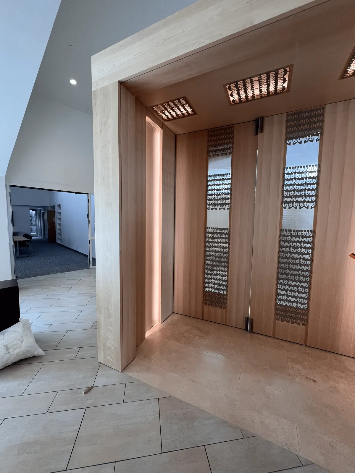 Side view of the Portal's wood pivot doors with patterned inserts and a lit jamb reveal