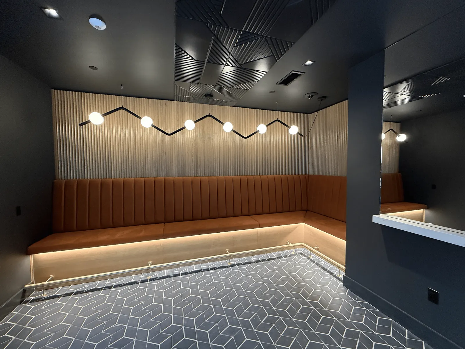 L-shaped banquette with a lit light-wood base and a brass foot rail beneath a fluted wood wall