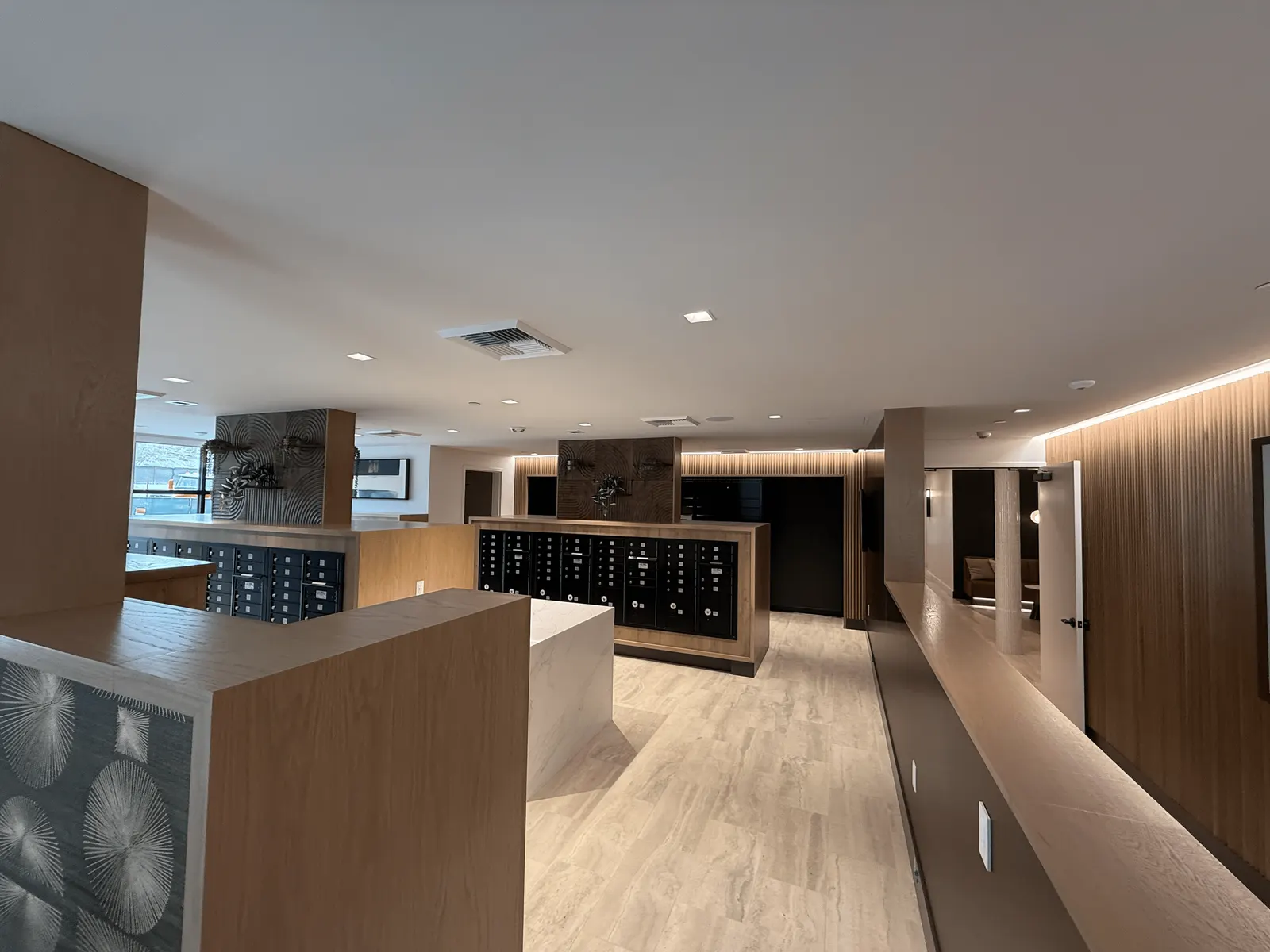 Mailroom with wood-clad mailbox enclosures, a white island and wood slat wall paneling under a lit cove