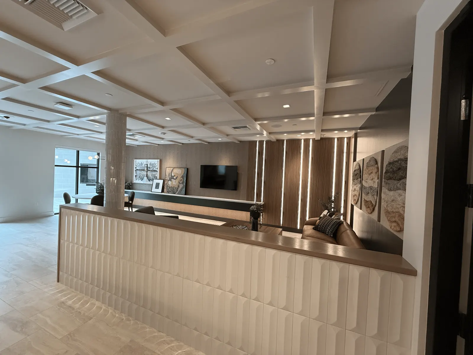Clubroom with a wood-capped half wall, a coffered ceiling and wood slat panels with light strips