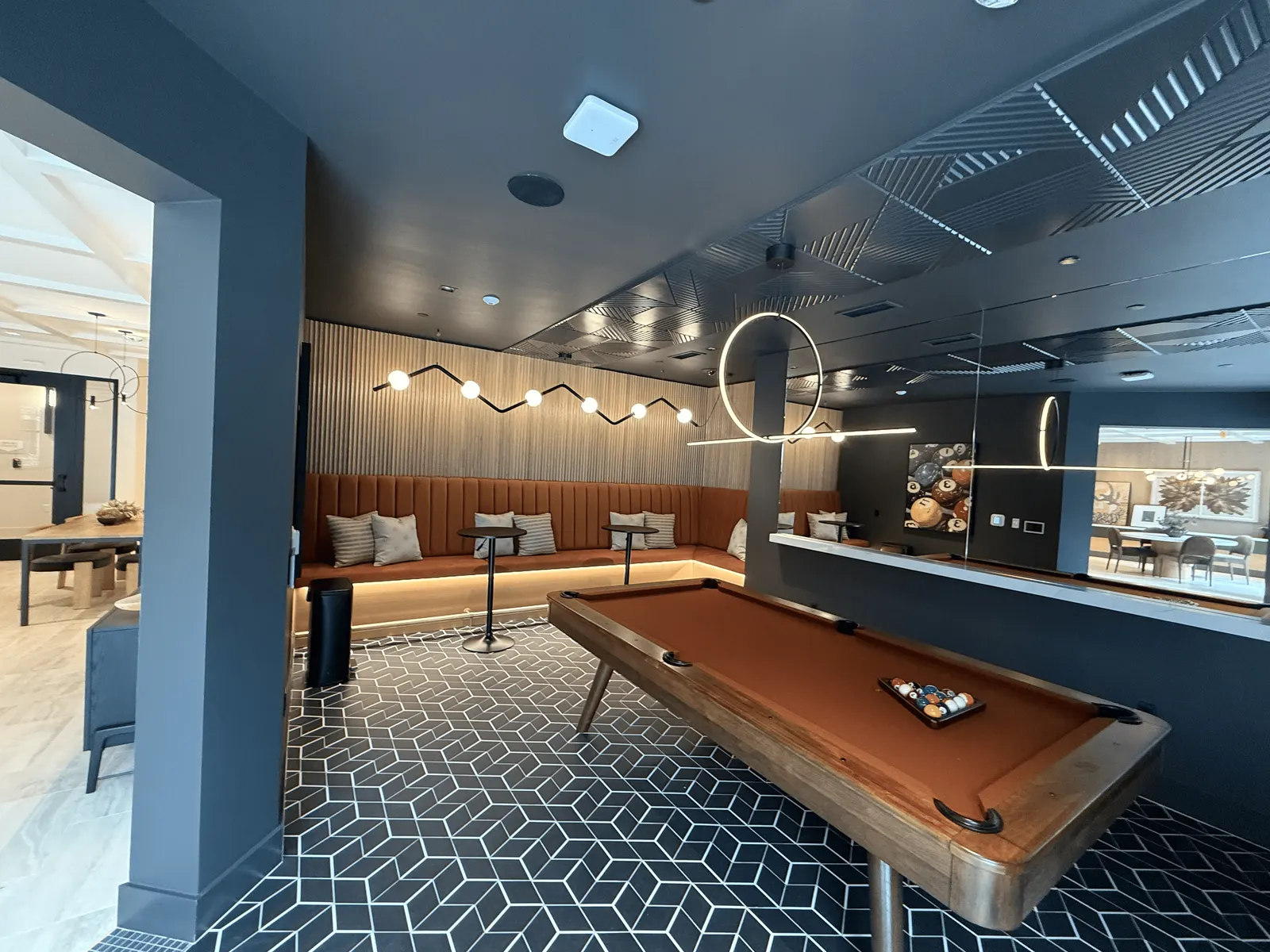Game lounge with a channel-tufted banquette on a lit wood base, fluted wall paneling and textured ceiling panels