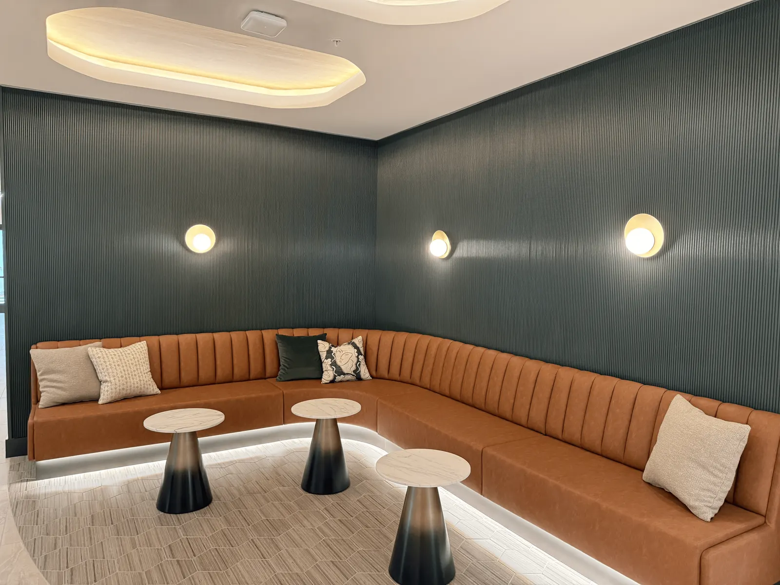 Curved upholstered banquette on a lit base against dark fluted wall paneling, under an oval light-wood ceiling panel