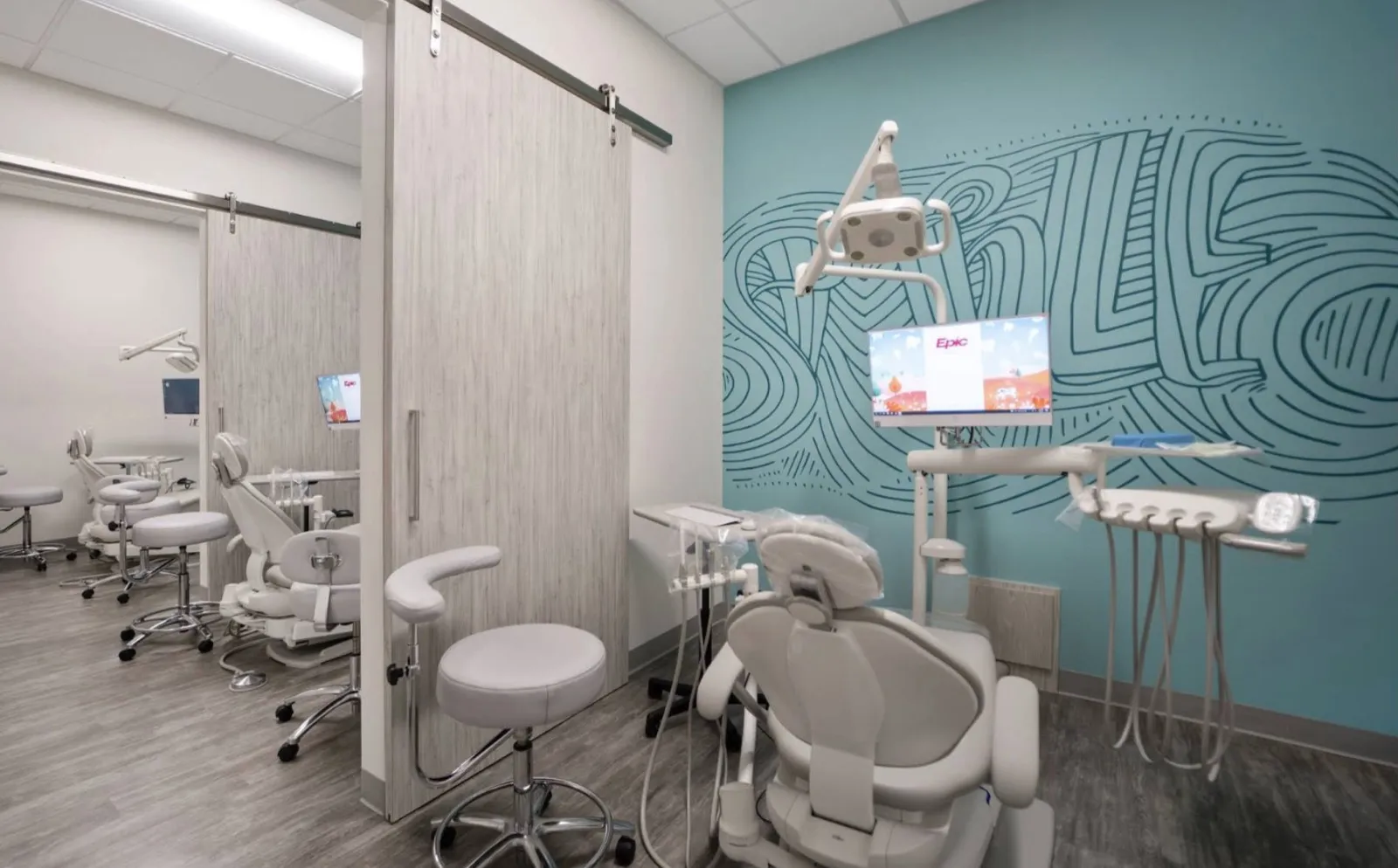 Finished treatment rooms at Dentists of Redding with dental chairs, sliding wood-look doors and a teal mural wall