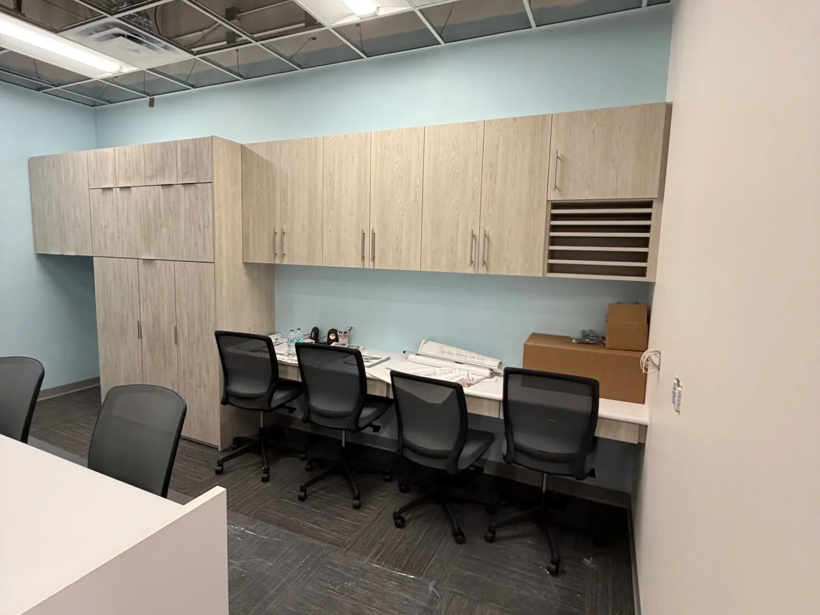 Wall of wood-look laminate upper cabinets, a tall cabinet and open mail slots above a long staff work surface in the front office