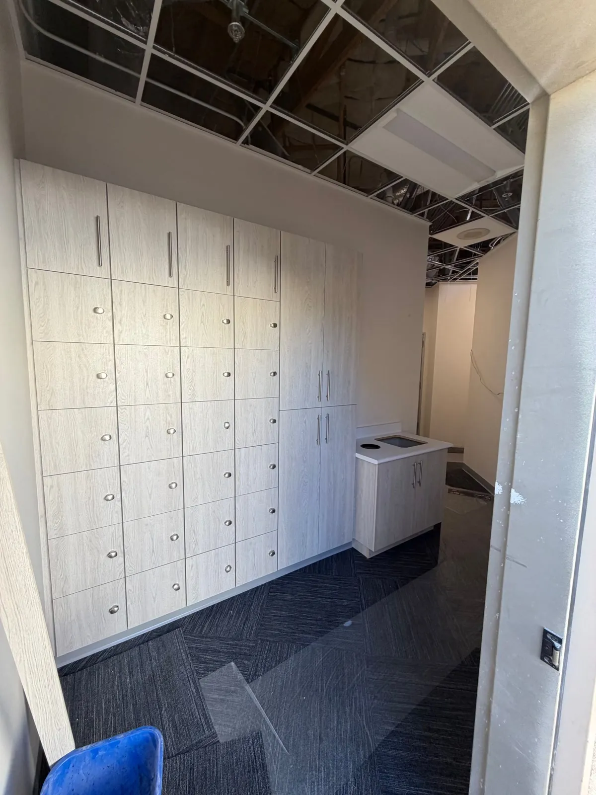 Wall of laminate locker cabinets with round pulls beside tall cabinets in a staff area