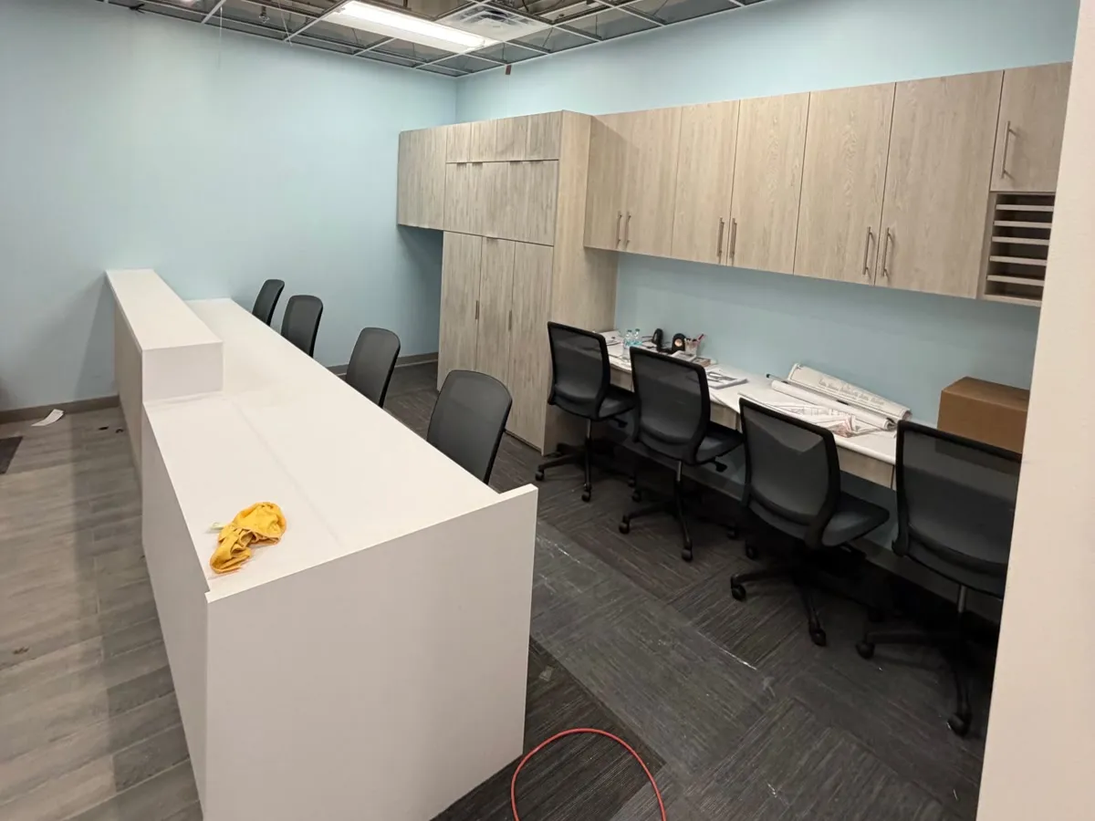 White reception transaction counter in front of wood-look laminate upper cabinets and a staff work surface at Dentists of Redding