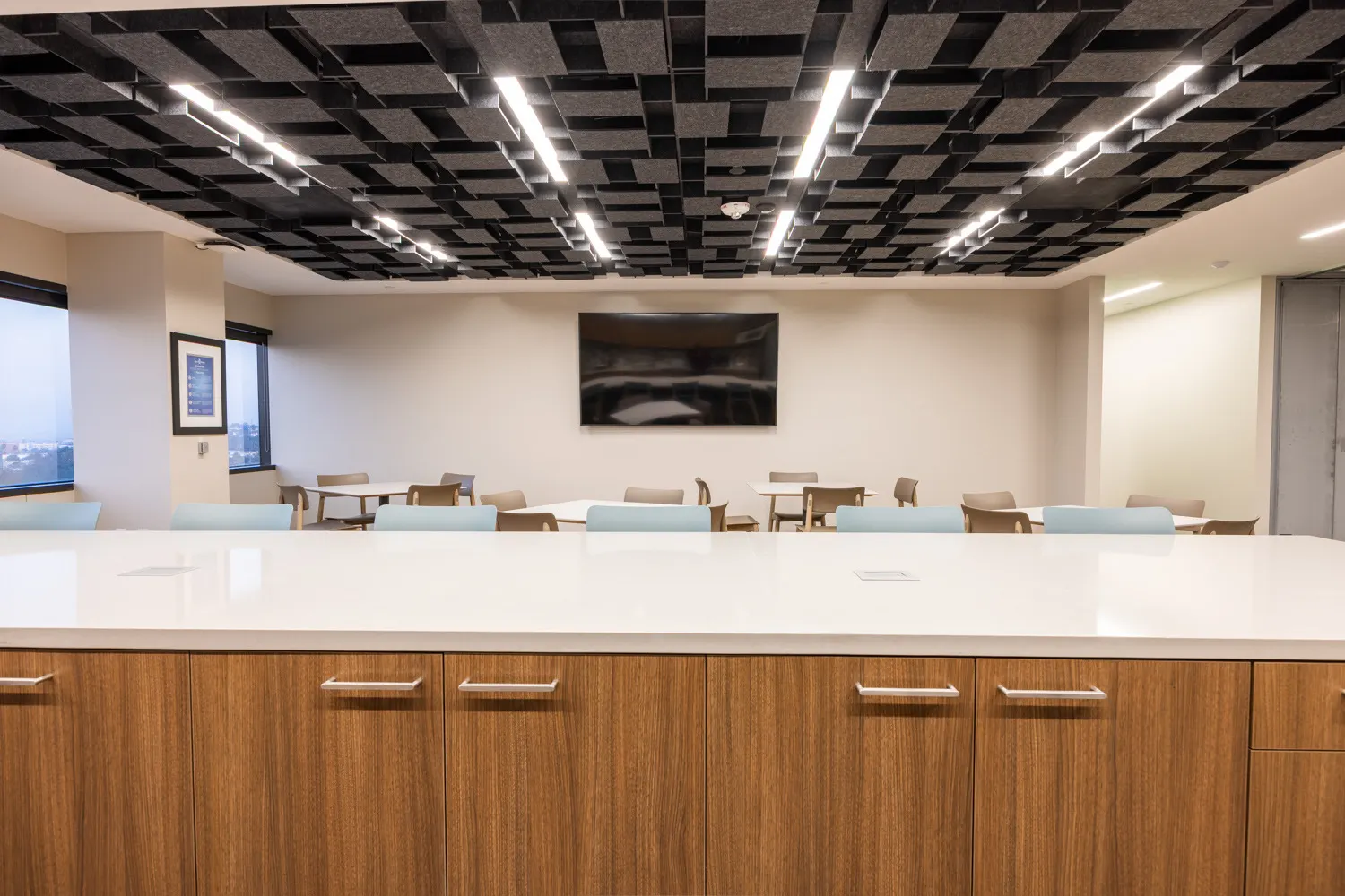 Row of wood-grain island base cabinets with long metal pulls under a white top, facing the lunchroom tables
