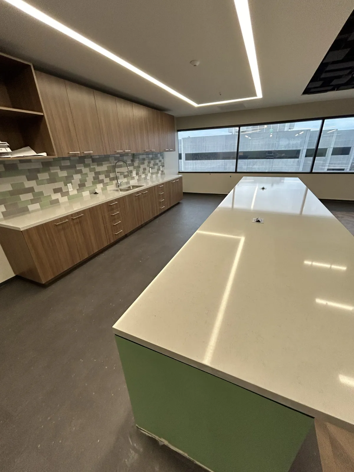 Pantry island with a white top and green end panel, wall cabinets and tile backsplash behind it