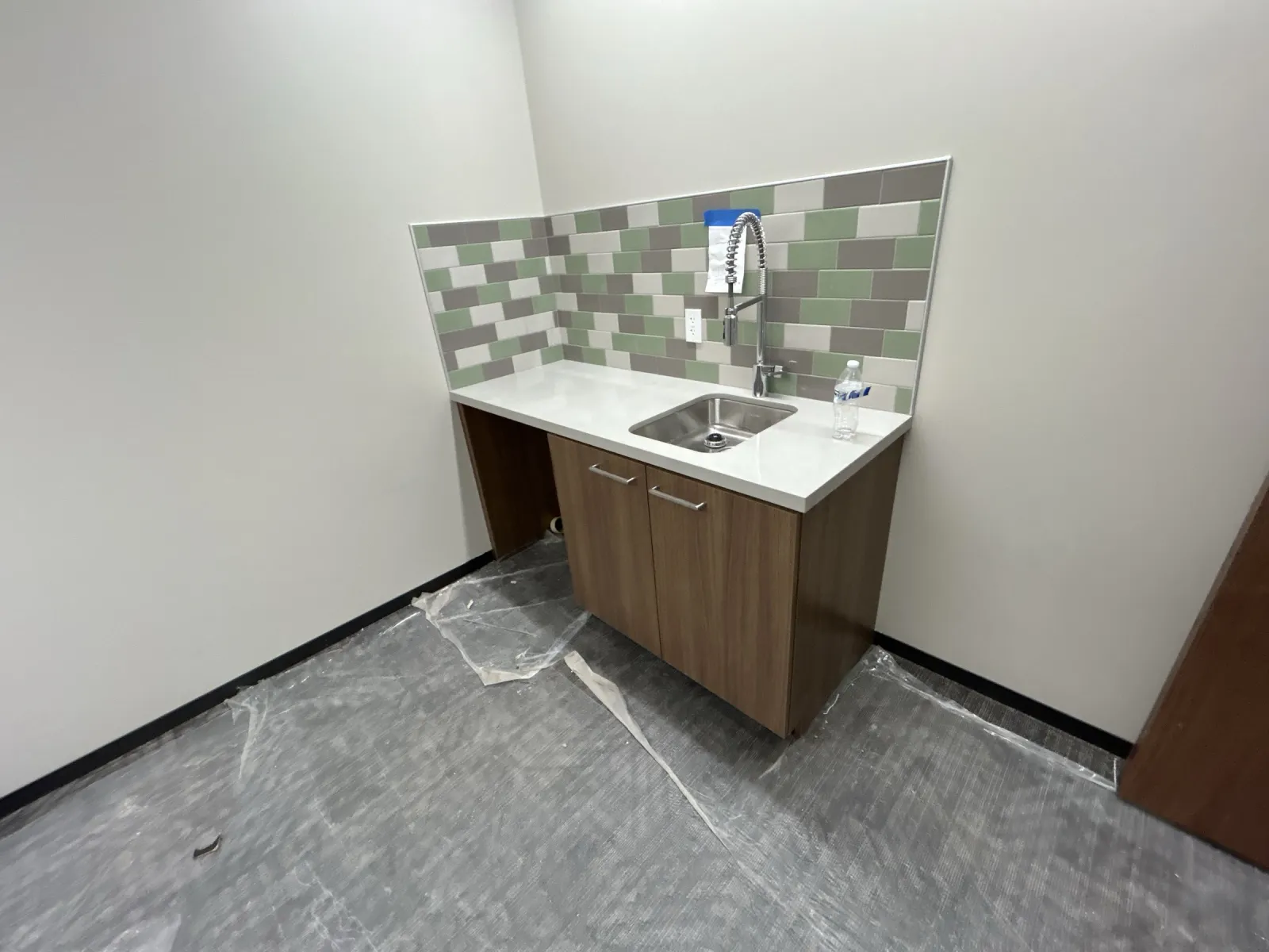 Wood-grain sink base cabinet under a white top with a tiled backsplash in a small support room