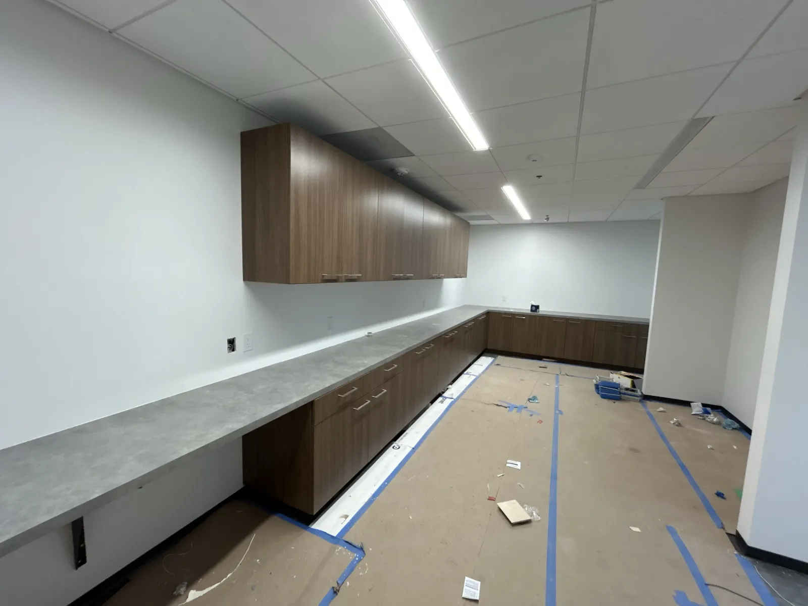 Long gray work counter on wood-grain base cabinets, with matching upper cabinets, in a support room