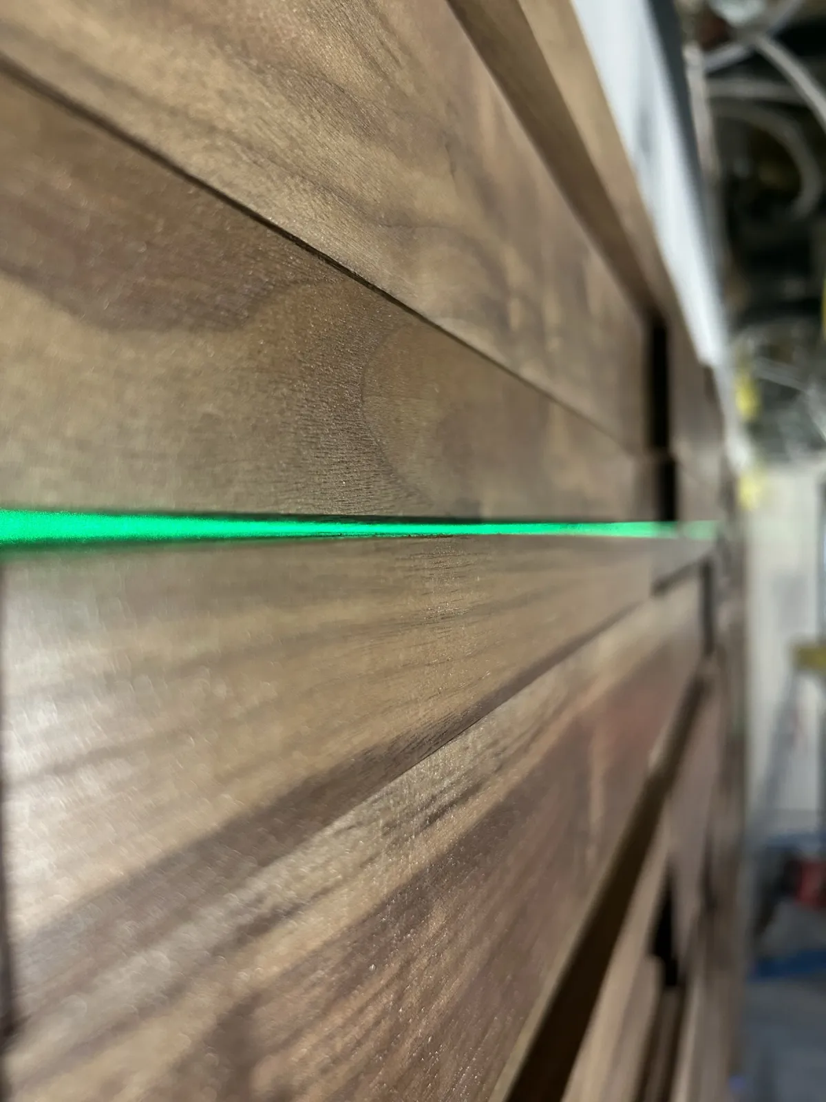 Close view of stepped solid-walnut courses on the ledge wall, a green laser level line across them