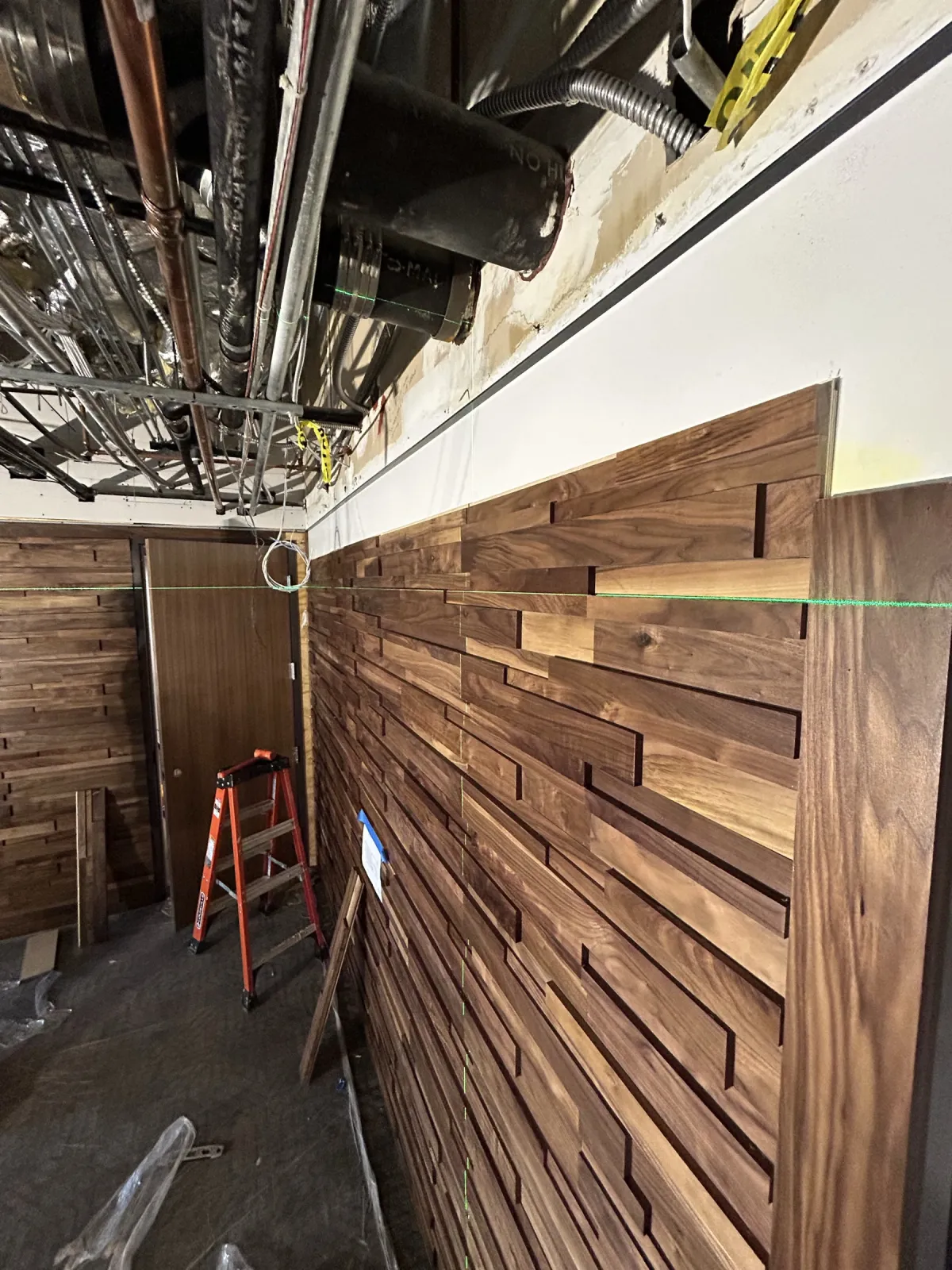 Solid-walnut ledge wall going up course by course, with a ladder and the open ceiling above
