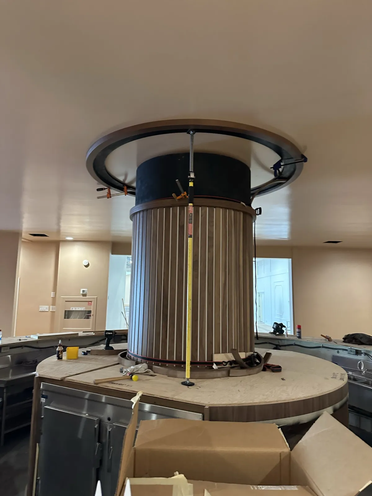 Close view of the circular bar's slatted walnut column inside its ring, with the canopy ring hanging above