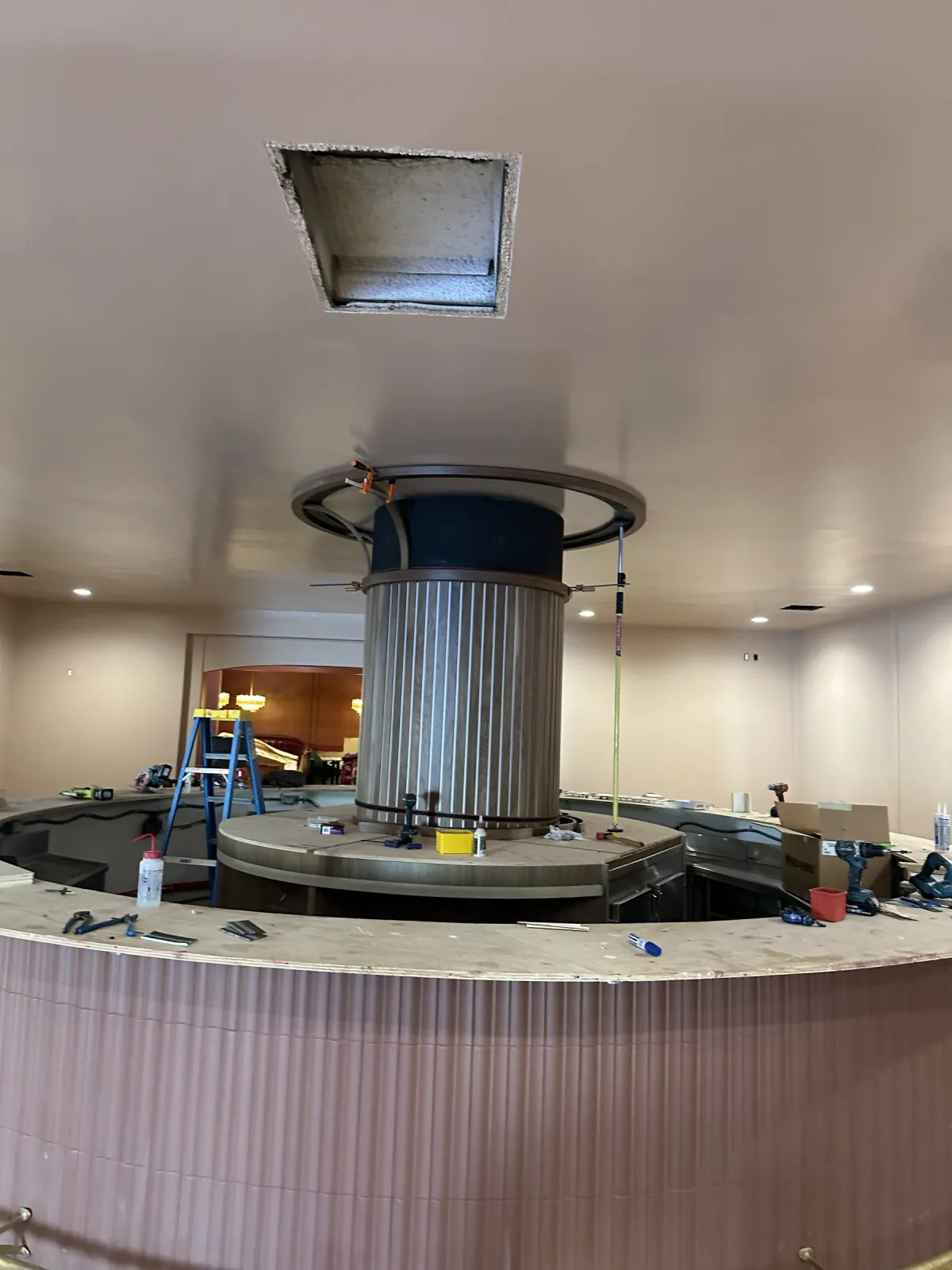 Circular bar during installation: slatted column wrapped around the center post, canopy ring above, tools on the top
