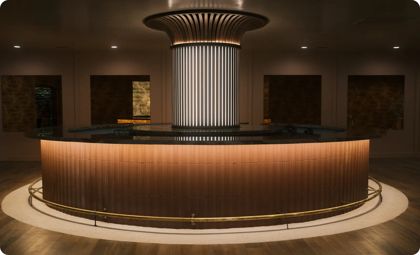 Circular bar at The Linden Club with a lit slatted center column, flared slatted canopy and brass foot rail