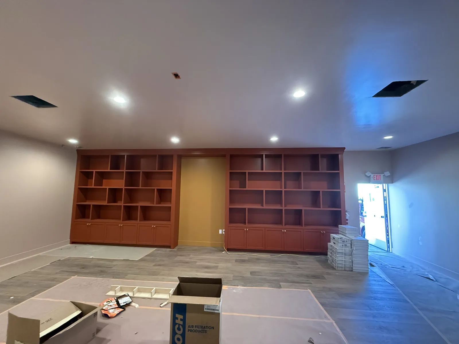 Library wall of stained open shelving and base cabinets on both sides of a central opening, room still under protection