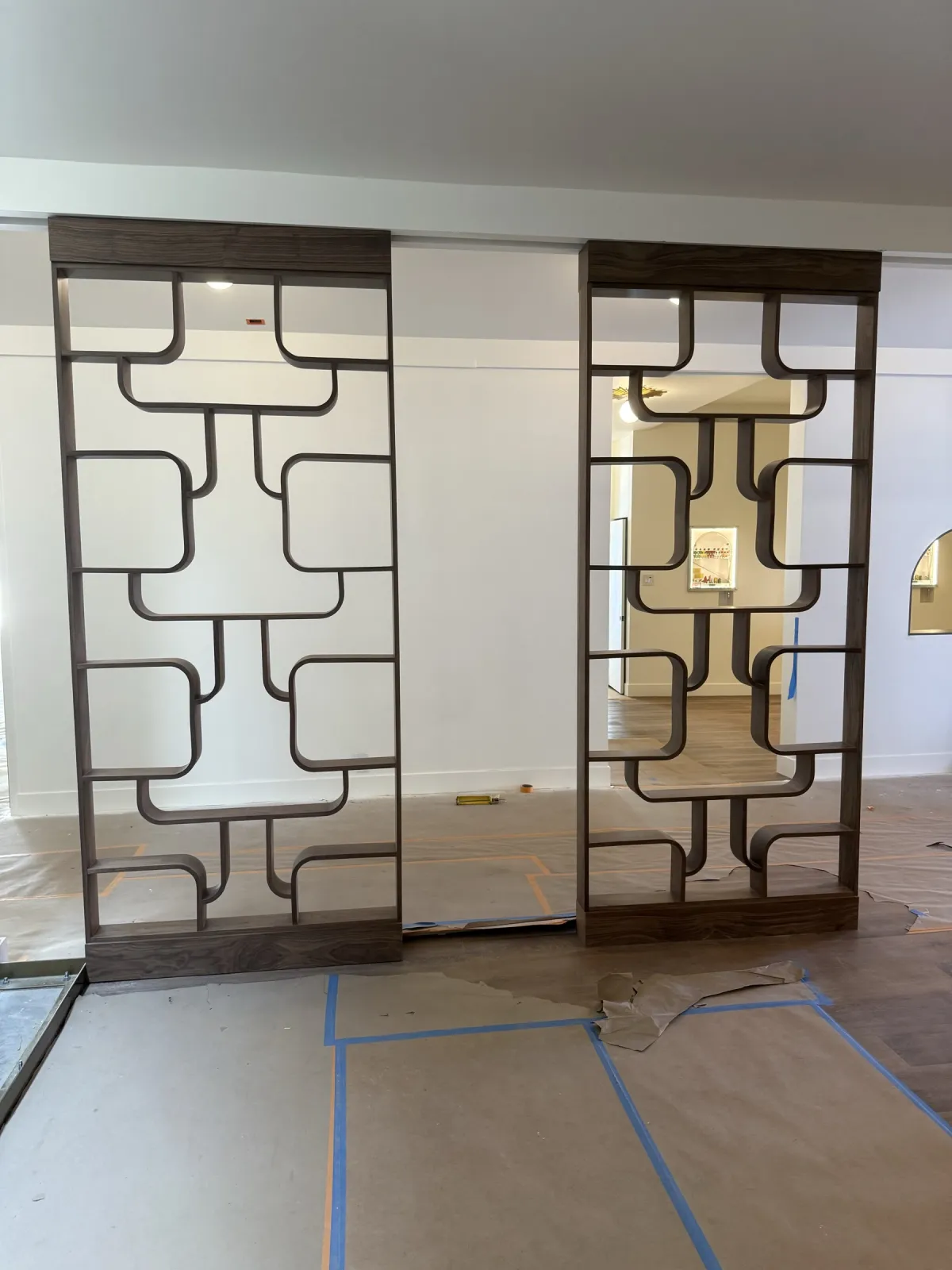 Two floor-to-ceiling walnut lobby screens with rounded rectangular openings, floor still under protection