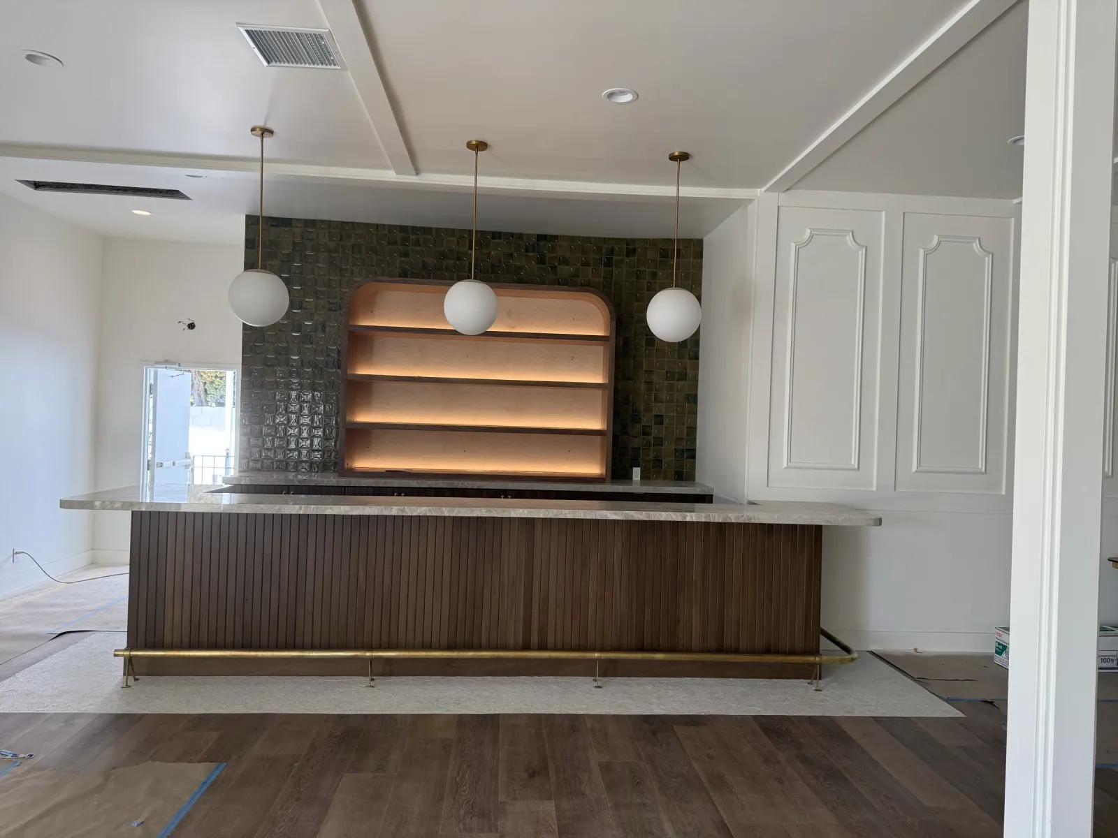 Terrace bar with a vertical-slat walnut front and brass foot rail, and an arched back wall with lit wood shelves