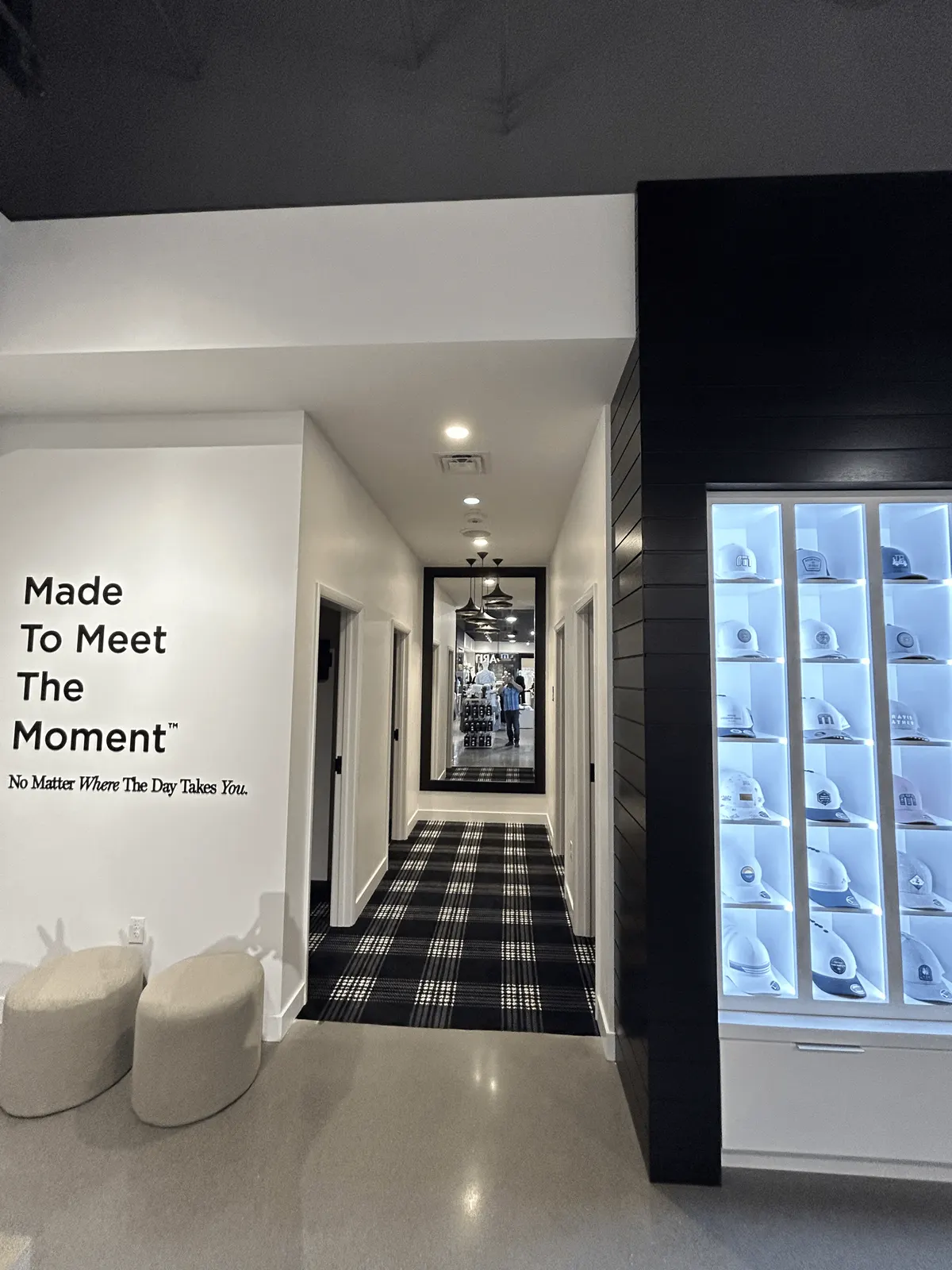Black horizontal wood cladding around a lit cap display wall, beside the fitting-room corridor