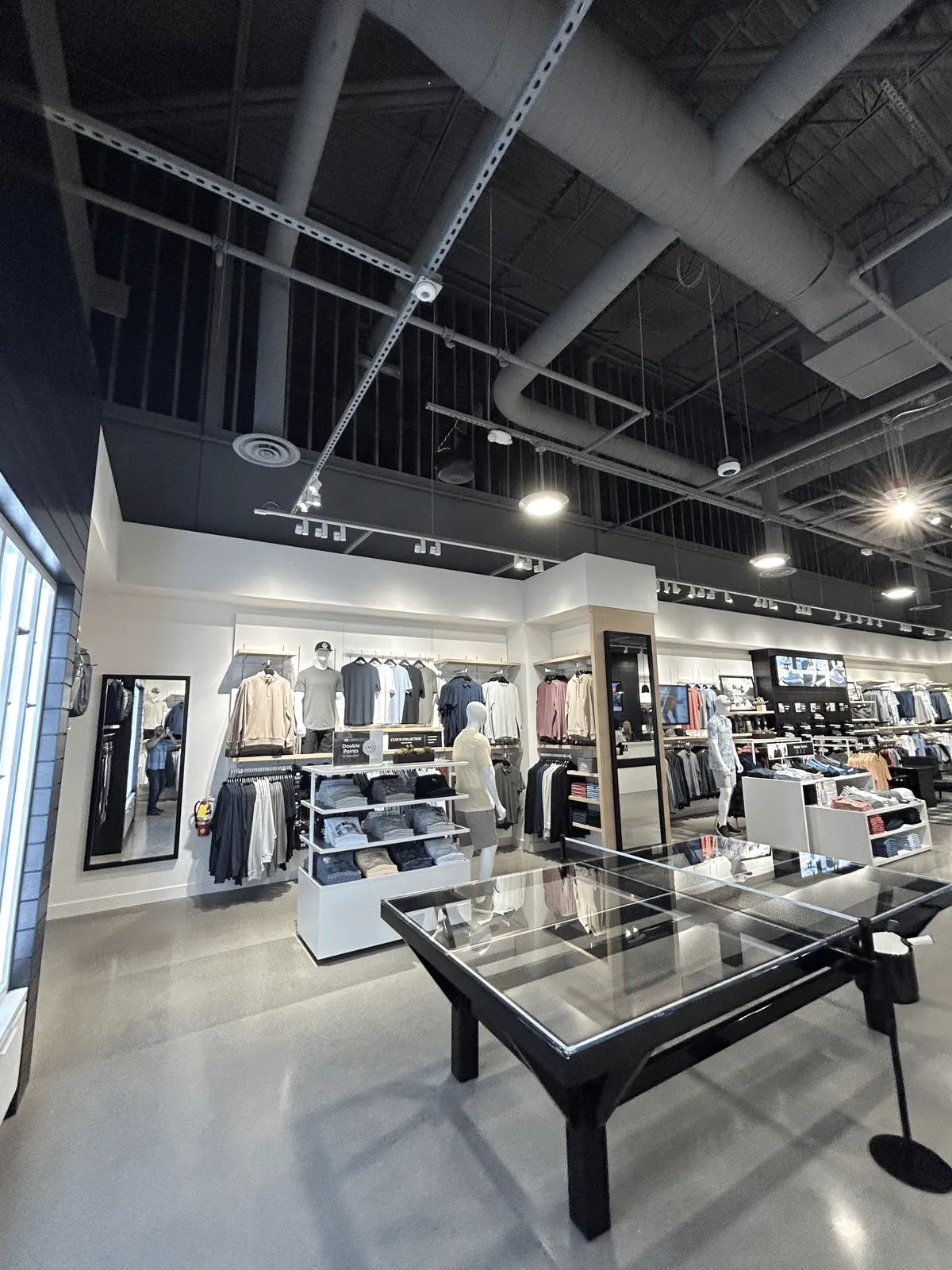 Sales floor with a wood-framed mirror column, white display fixtures and garment walls under an open ceiling