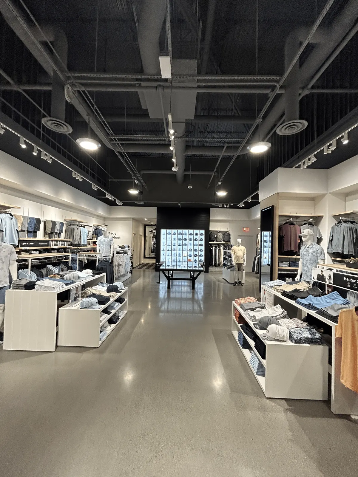 Sales floor with white merchandise tables and light wood wall shelving leading to a lit cap display