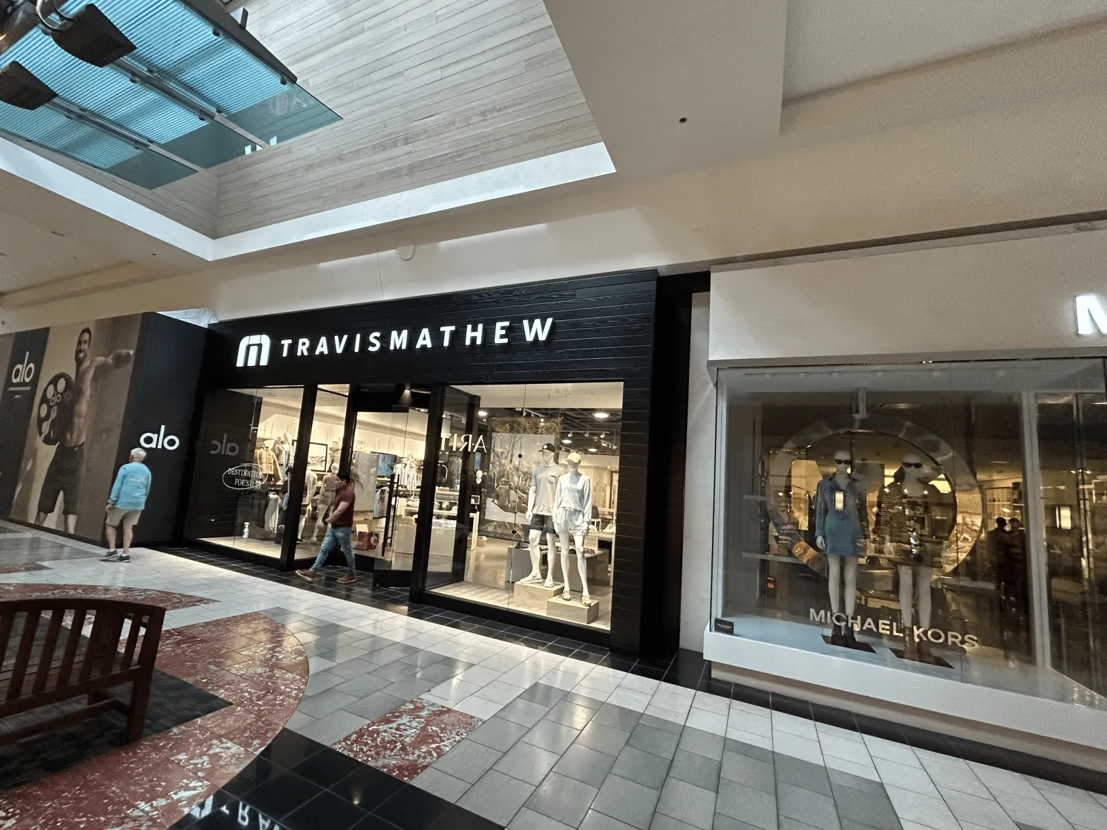 TravisMathew storefront at Washington Square: black horizontal wood cladding, lit sign and full-height glass entrance